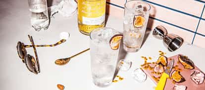 Absolut Passionfruit Fizzy in a highball glass with ice and a passionfruit slice, bottle and bar tools on tiled counter