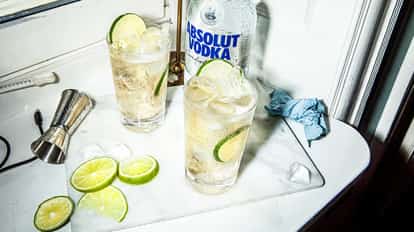 How to Prepare and Drink Vodka: Two vodka cocktails with lime and ice on a marble countertop beside a bottle of Absolut Vodka and bar tools.