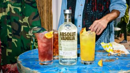 A bottle of Absolut Vanilia with a cocktail on either side of it, and in the background, a man in a blue shirt visible from the neck down.