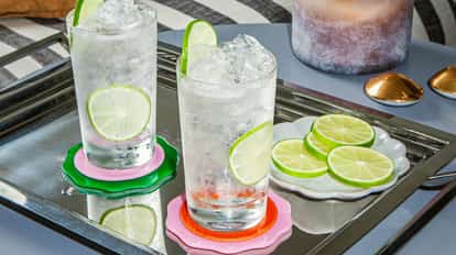 Absolut Lime Soda with ice and lime slices in tall glasses on a mirrored tray with colorful coasters and extra citrus slices.