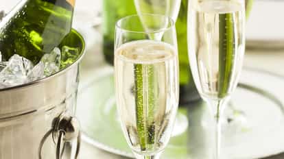 Chilled bottle of sparkling wine in an ice bucket next to two filled champagne flutes on a silver tray.