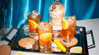Absolut Peach with Iced Tea three glasses with ice and lemon slices beside a peach vodka bottle on a tray