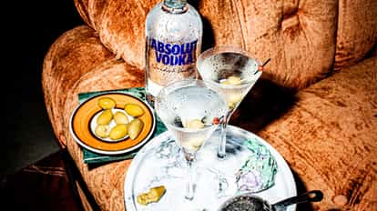 Absolut Martini served in two chilled martini glasses garnished with olives and a vodka bottle on a couch