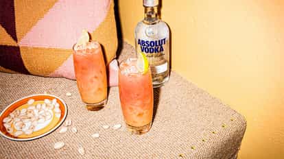Absolut vodka bottle beside two highball glasses of pink cocktails garnished with lime