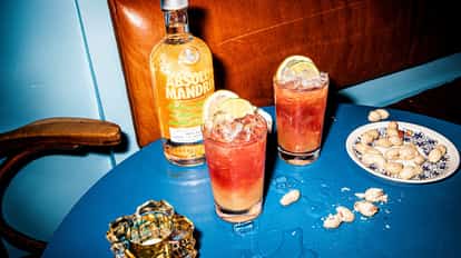 Two punch cocktails in highball glasses with lime wheels beside an Absolut Mandrin bottle on a blue table