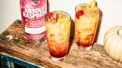 Absolut Raspberri Sunrise cocktail next to a bottle of Absolut Raspberri vodka.