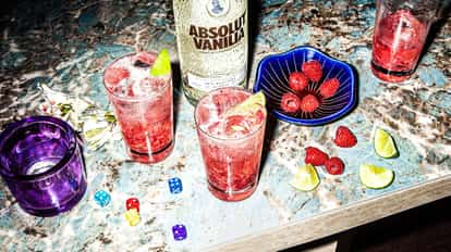 Absolut Vanilia In The Sky in a highball glass with crushed ice lime wedge and raspberries on marble countertop