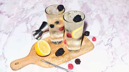 Absolut Wild Berri Lemonade served in two highball glasses with crushed ice, lemon slice and berries on a wooden board