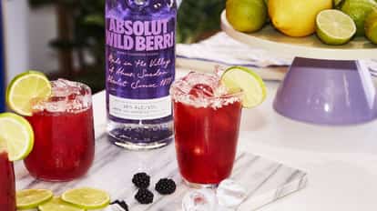 Absolut Wild Berri Vodkarita served in salted highball glasses with lime wedges beside a bottle.