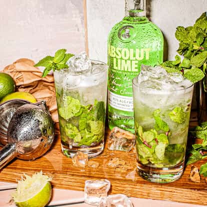 Two Lime Mojito cocktail served in highball glasses garnished with mint and lime standing on a tray in wood