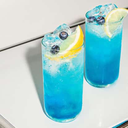 Blueberry Fizz cocktails served in tall, chilled glasses, vibrant blue and packed with ice, garnished with lemon wedges and fresh blueberries.