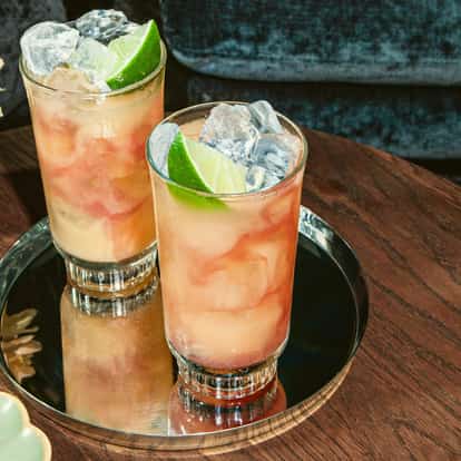 Absolut vodka bottle beside two highball glasses of pink cocktails garnished with lime