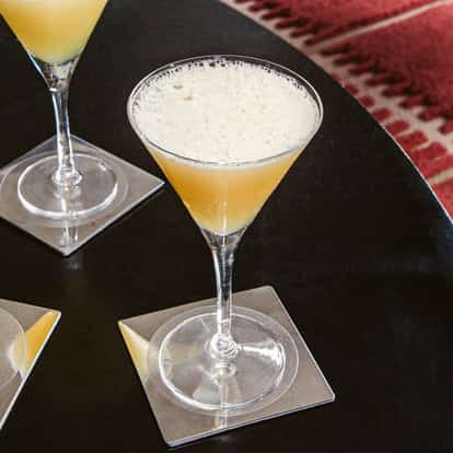 Absolutely Bananas cocktails served in chilled martini glasses with a light, frothy top, set on a dark table with clear square coasters.