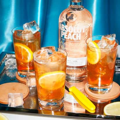 Absolut Peach with Iced Tea three glasses with ice and lemon slices beside a peach vodka bottle on a tray