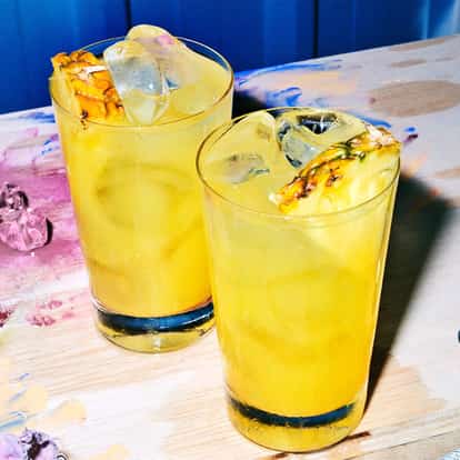 Absolut Long Pornstar in two highball glasses with ice and pineapple wedges on a paint-splattered wooden board