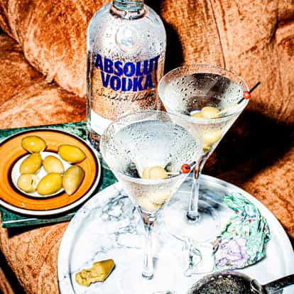 Absolut Martini served in two chilled martini glasses garnished with olives and a vodka bottle on a couch