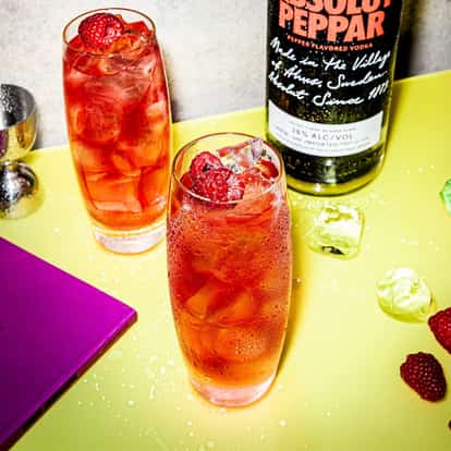 Two glasses with Absolut Peppar Alert standing on a table beside an Absolut Peppar bottle.