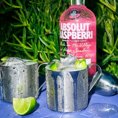 Raspberry Vodka Mule in two metal mugs with ice and lime wedges and an Absolut Raspberri bottle behind