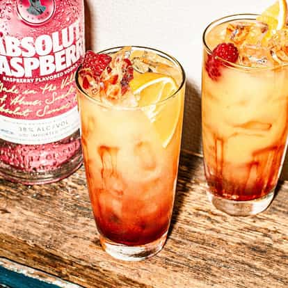 Absolut Raspberri Sunrise cocktail next to a bottle of Absolut Raspberri vodka.