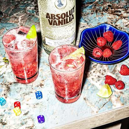 Absolut Vanilia In The Sky in a highball glass with crushed ice lime wedge and raspberries on marble countertop