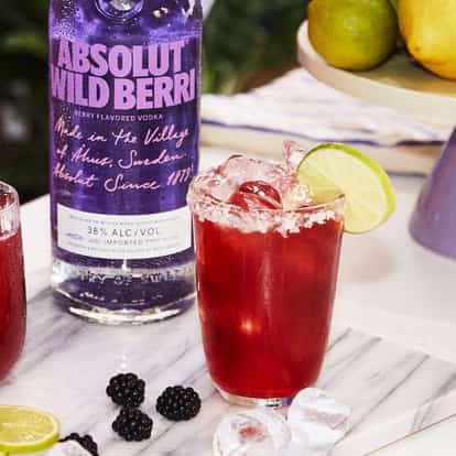 Absolut Wild Berri Vodkarita served in salted highball glasses with lime wedges beside a bottle.