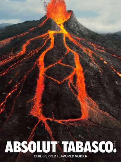 Erupting volcano with glowing lava flows forming an Absolut Vodka bottle and cross shape, flanked by Absolut and Tabasco logos; text reads “Chili Pepper Flavored Vodka.”