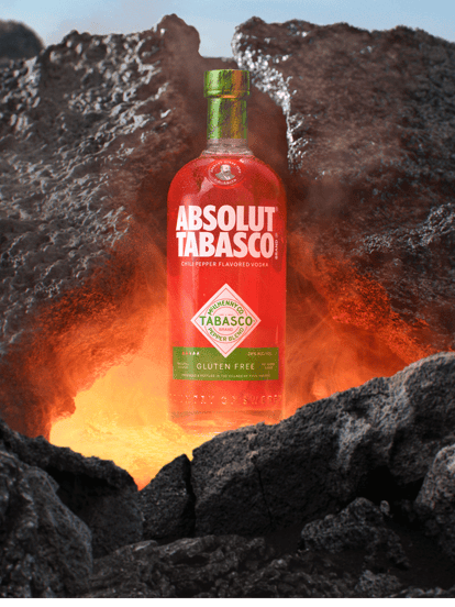 ABSOLUT® TABASCO™ chili pepper flavored vodka bottle emerging from molten lava between dark volcanic rocks, glowing with heat and intensity.