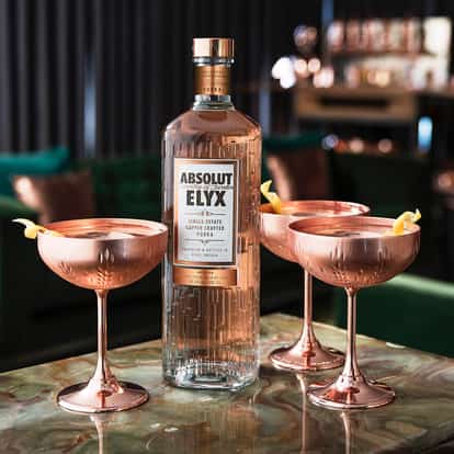 Absolut Elyx bottle on a bar with 3 copper martini glasses.