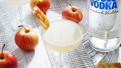 Apple Martini aka Appletini next to a bottle of Absolut Vodka and surrounded by red apples.