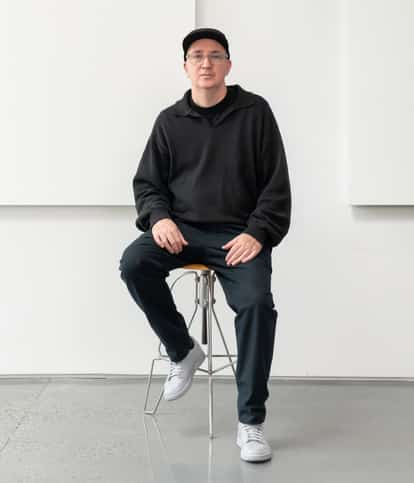 KAWS seated on a stool in his studio
