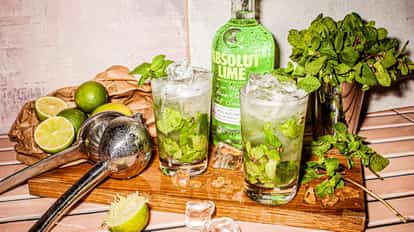 Two Lime Mojito cocktail served in highball glasses garnished with mint and lime standing on a tray in wood