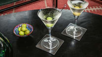 Absolut Martini served in two chilled martini glasses garnished with olives and a vodka bottle on a couch