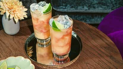 Absolut vodka bottle beside two highball glasses of pink cocktails garnished with lime