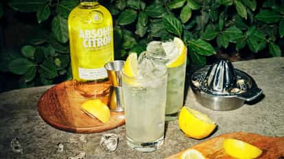 Absolut Citron Lemonade two tall glasses with ice and lemon wedges beside a bottle labeled Citron and a juicer