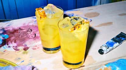 Absolut Long Pornstar in two highball glasses with ice and pineapple wedges on a paint-splattered wooden board