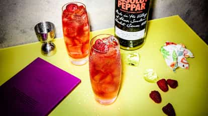 Two glasses with Absolut Peppar Alert standing on a table beside an Absolut Peppar bottle.