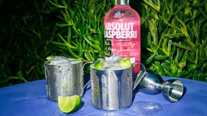 Raspberry Vodka Mule in two metal mugs with ice and lime wedges and an Absolut Raspberri bottle behind