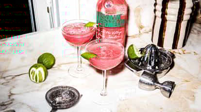 Cosmopolitan cocktails made with Absolut Watermelon next to a bottle of Absolut Watermelon.