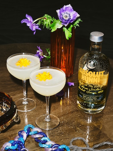 Image of new Absolut Hunni bottle presented on a round wooden table compained with 2 coupe glasses of Absolut Hunni lemon drop cocktail.